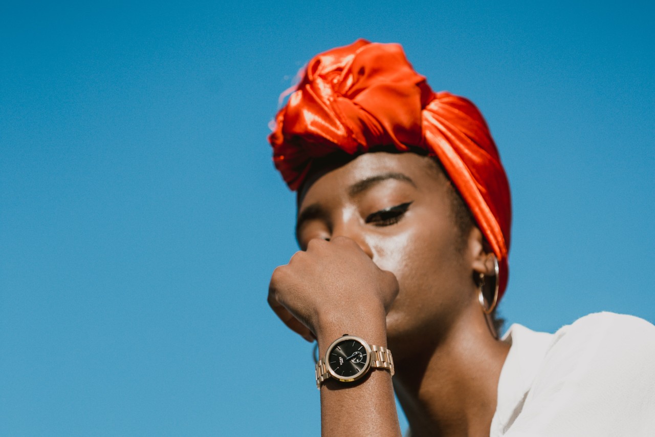 Close up of a woman in a red head wrap wearing a gold and black watch