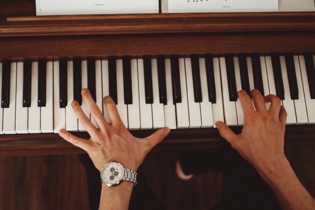 Hands playing a piano with a silver and white watch on the left wrist
