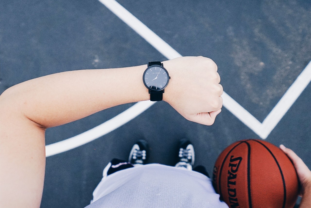A person checking their black toned watch during a basketball game