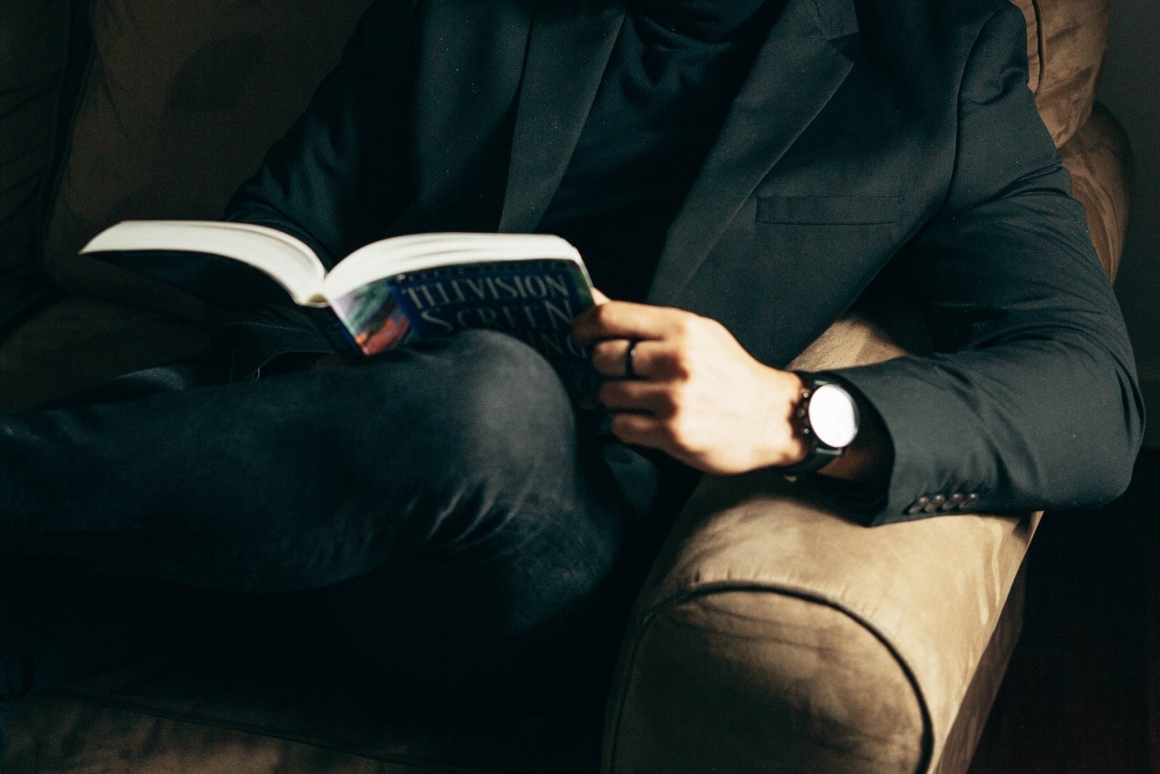 A man reading on the couch with a black dress watch