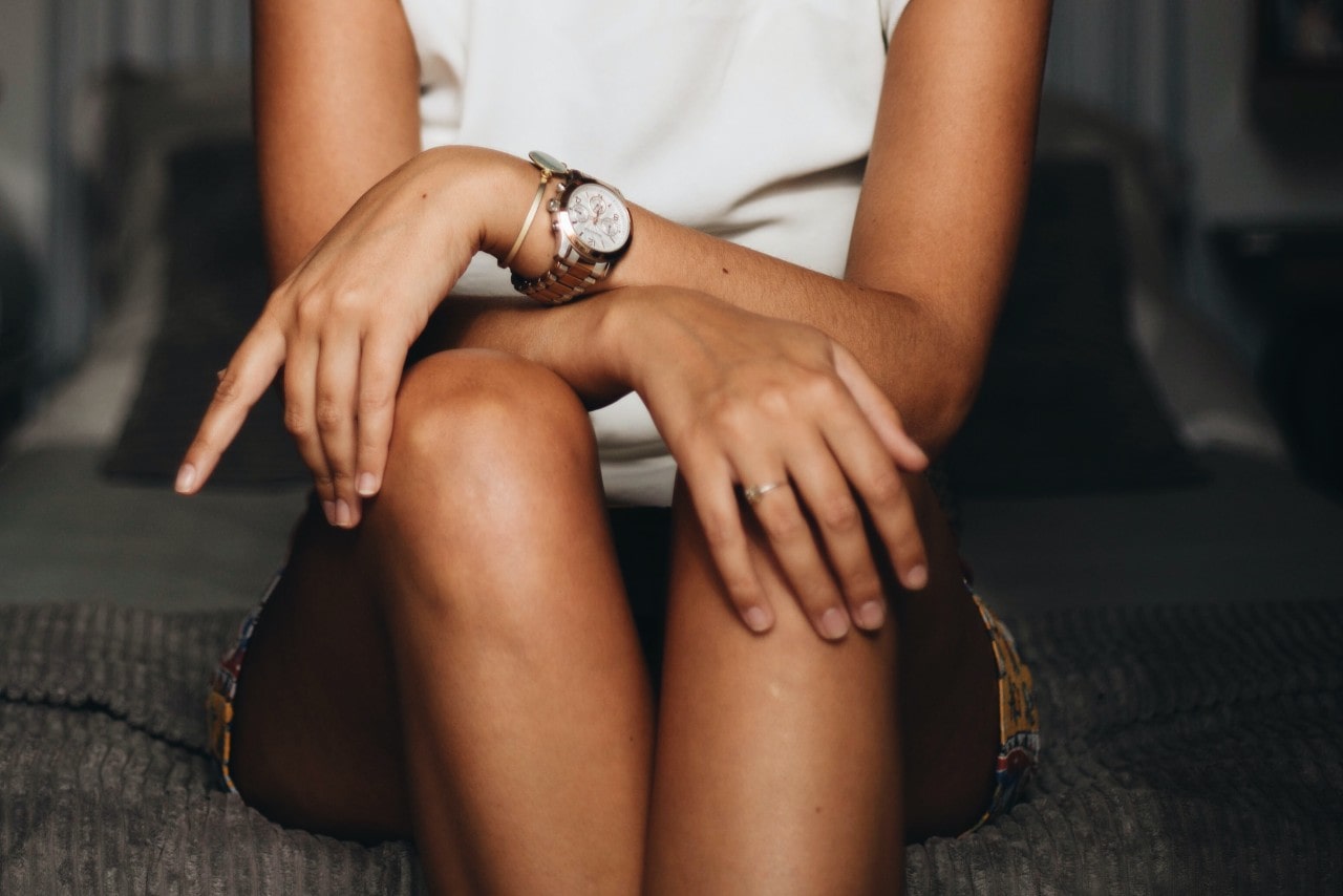 Woman sitting on edge of the bed with a gold watch and bracelet on