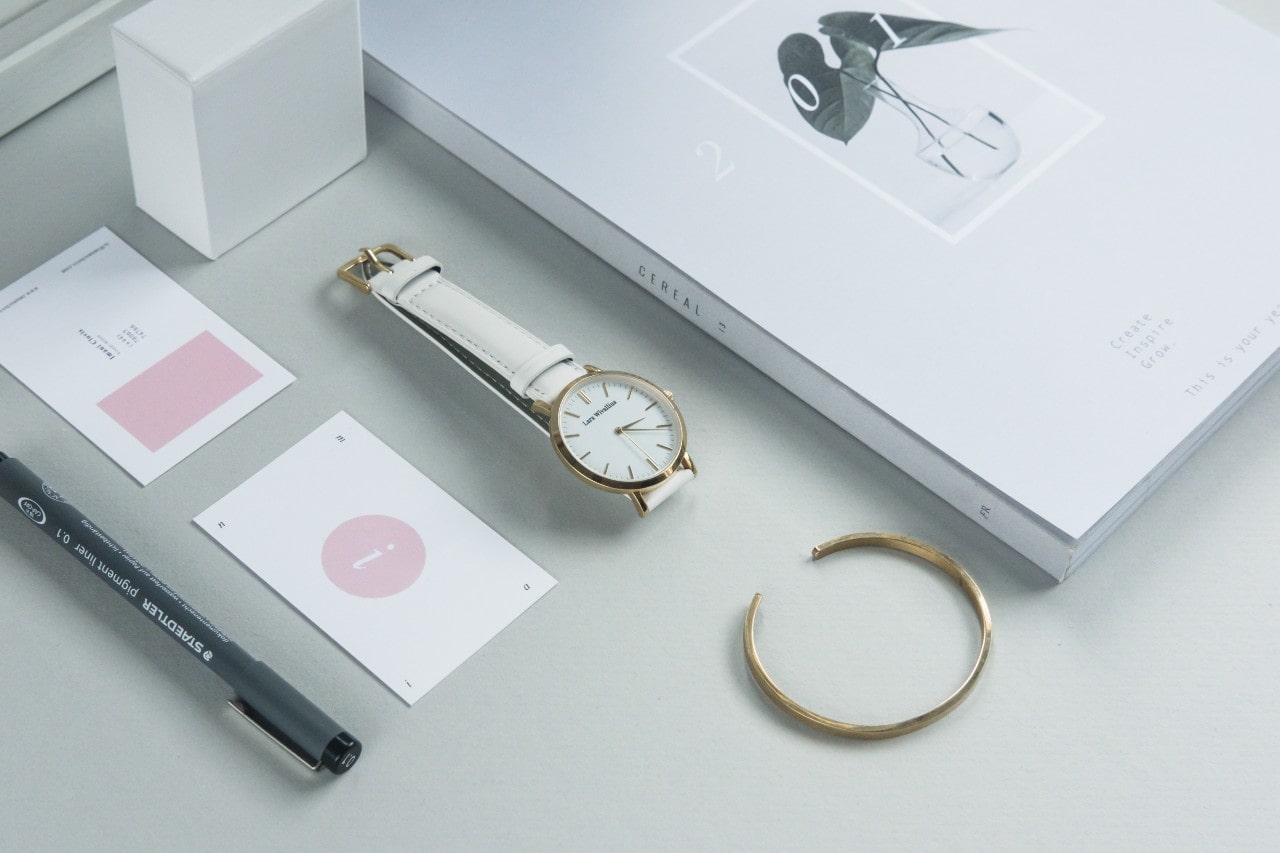 A woman sets down her white leather watch and yellow gold cuff on her desk