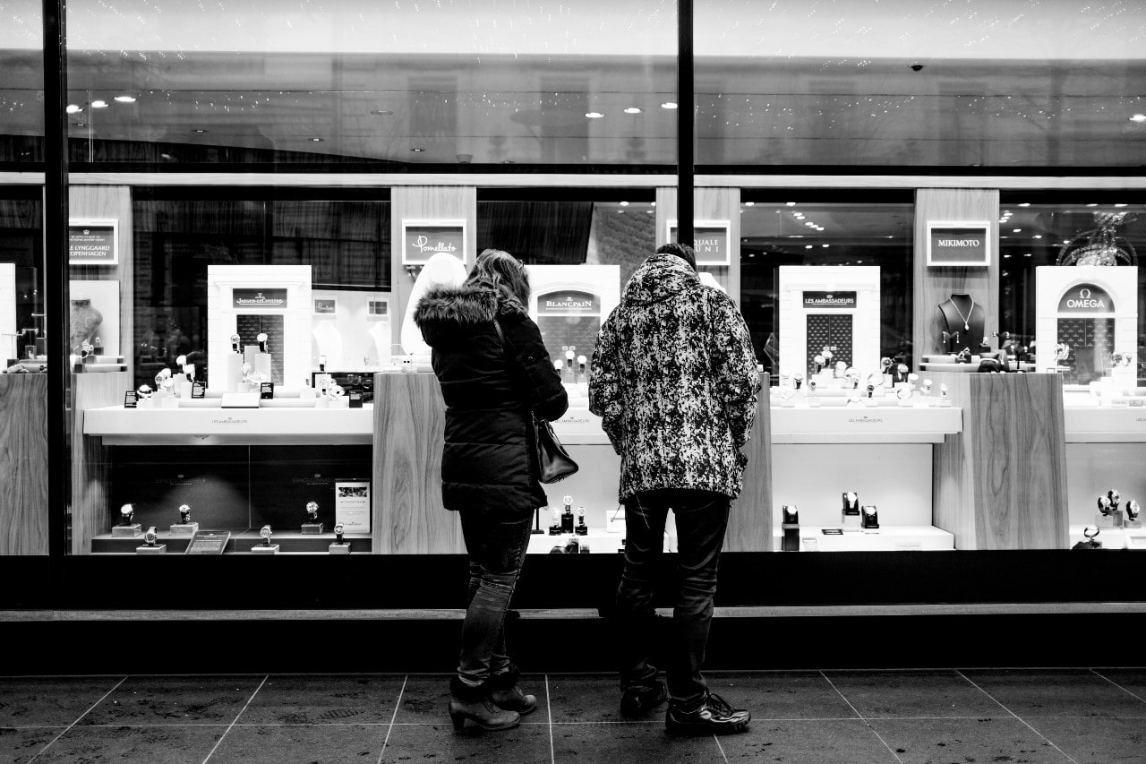 A couple looks into the display window of a closed jewelry store to get an idea of what their inventory looks like