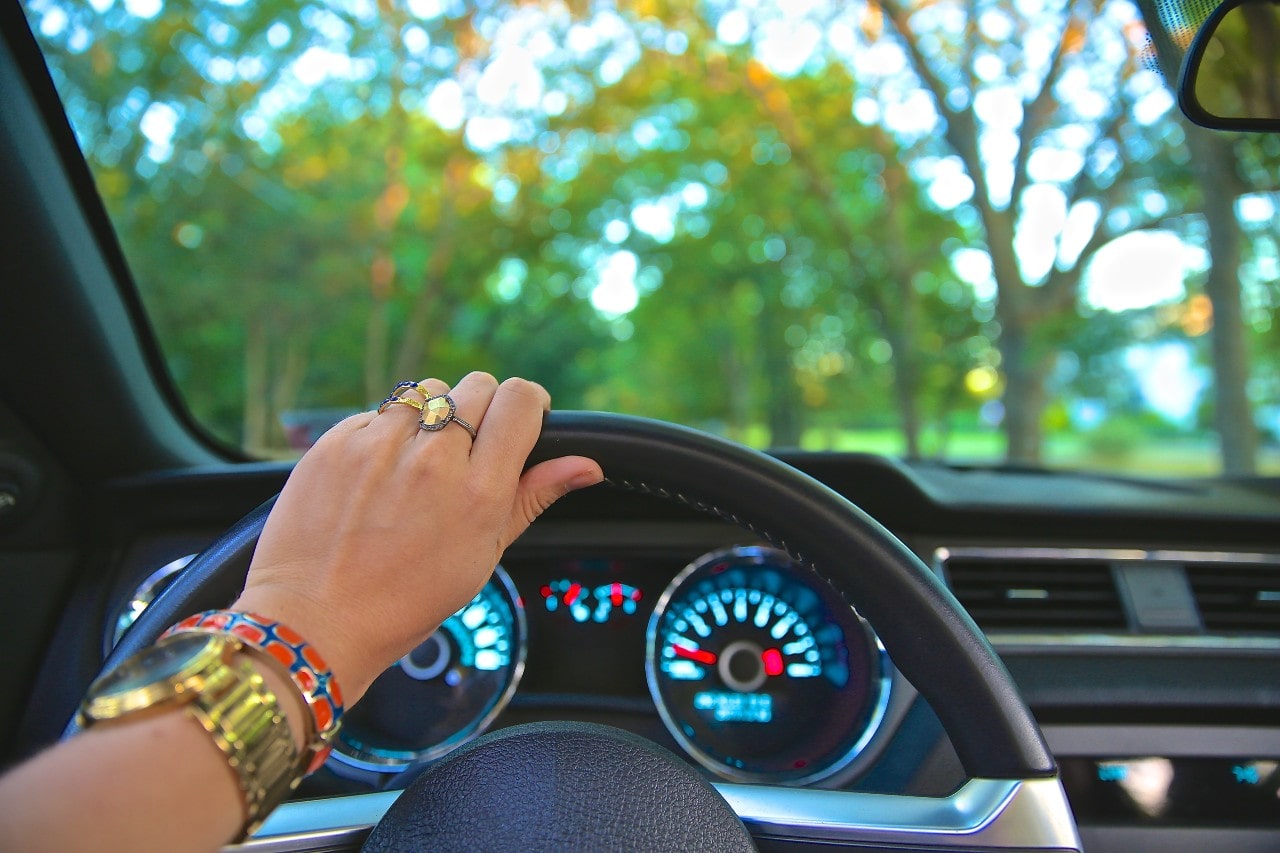 A woman wearing an array of gold and colorful jewelry, including a yellow gold watch, drives to her nearest jewelry store