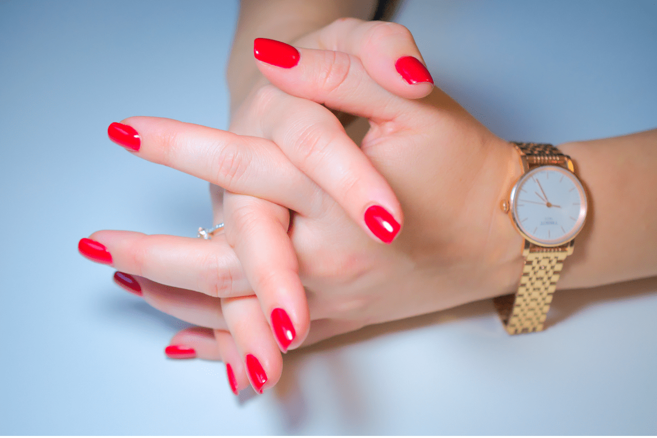 Woman with long red fingernails crossing her hands wearing a slender wristwatch