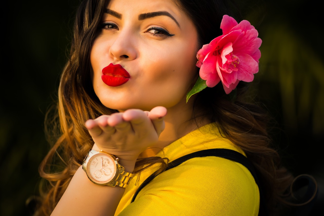 A woman blowing a kiss to the camera, wearing a yellow top and a white and gold timepiece