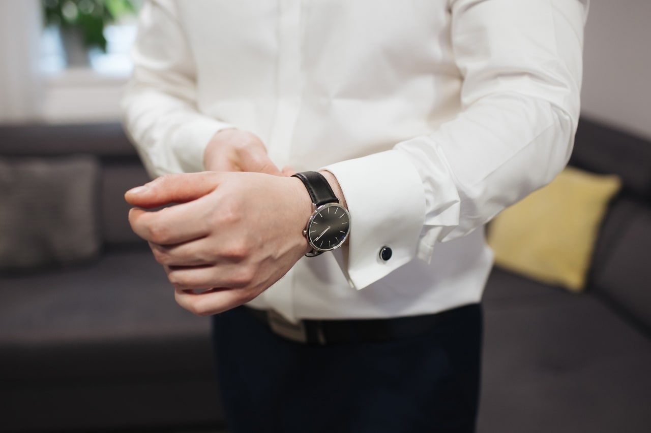 A man in a white dress shirt adjusting his black watch with a silver case
