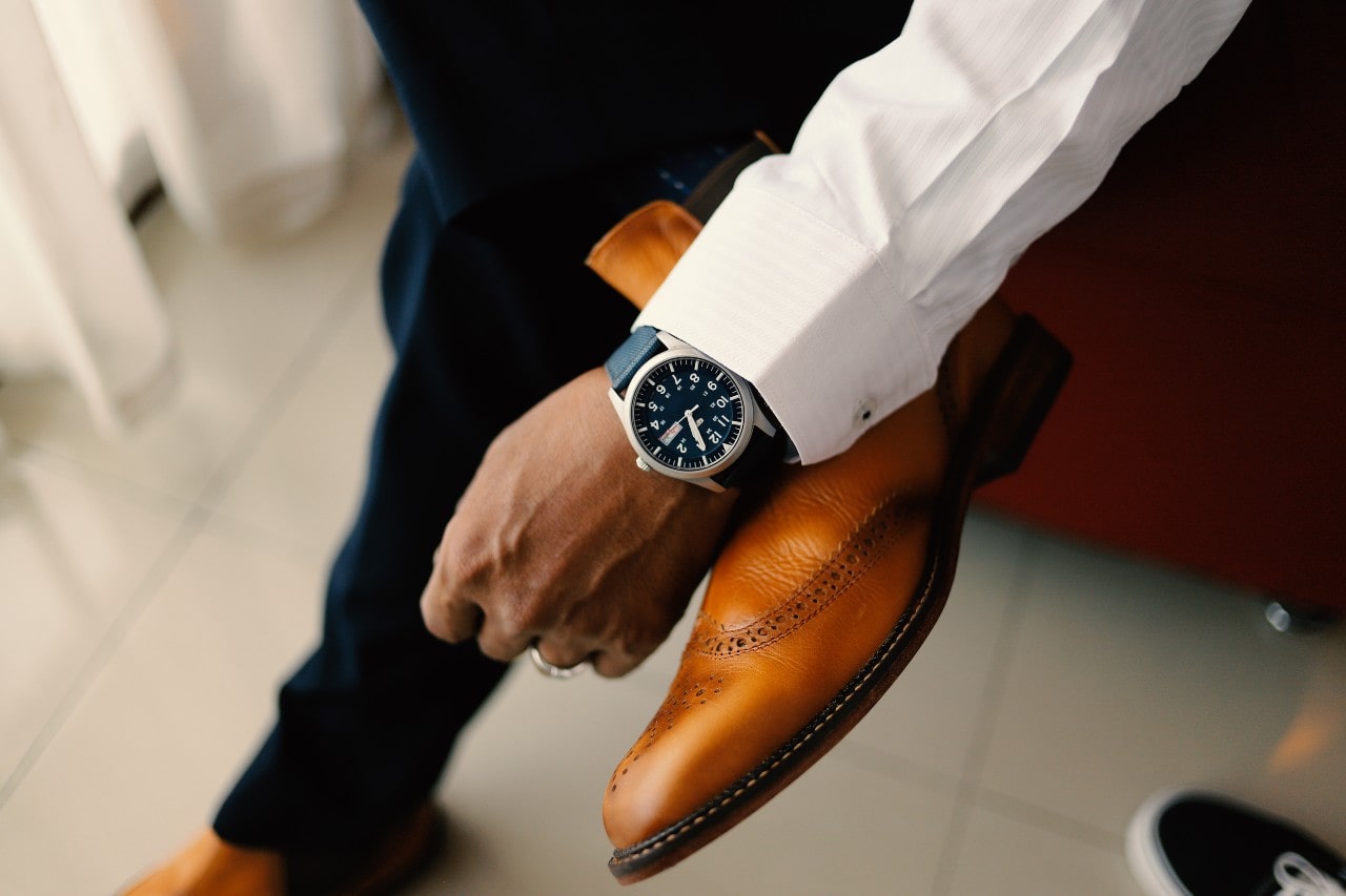 Man sitting with his leg across his other showing his dress shoes and timepiece