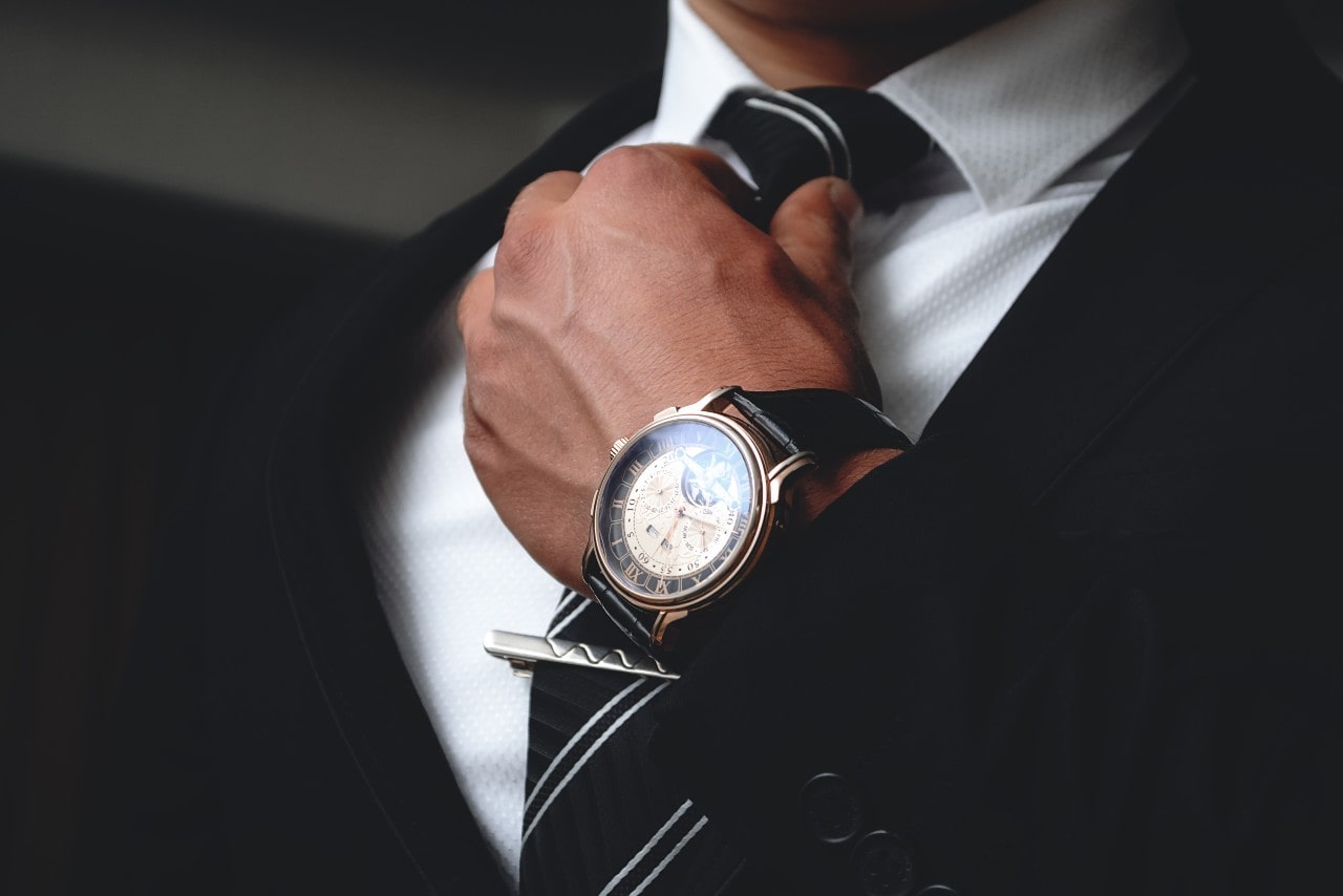 A man in a suit adjusts his tie, showing off his watch