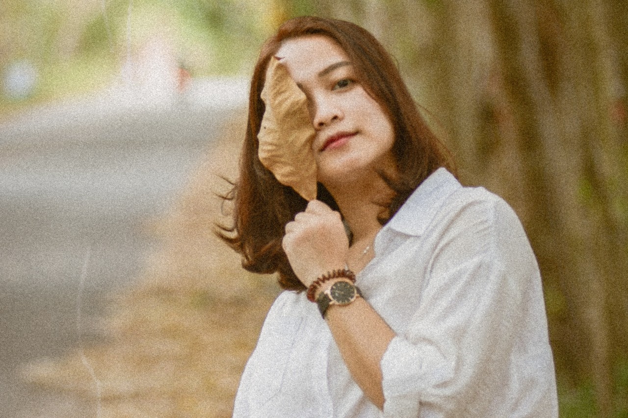 A woman holding a fall leaf to her face and wearing a yellow gold watch