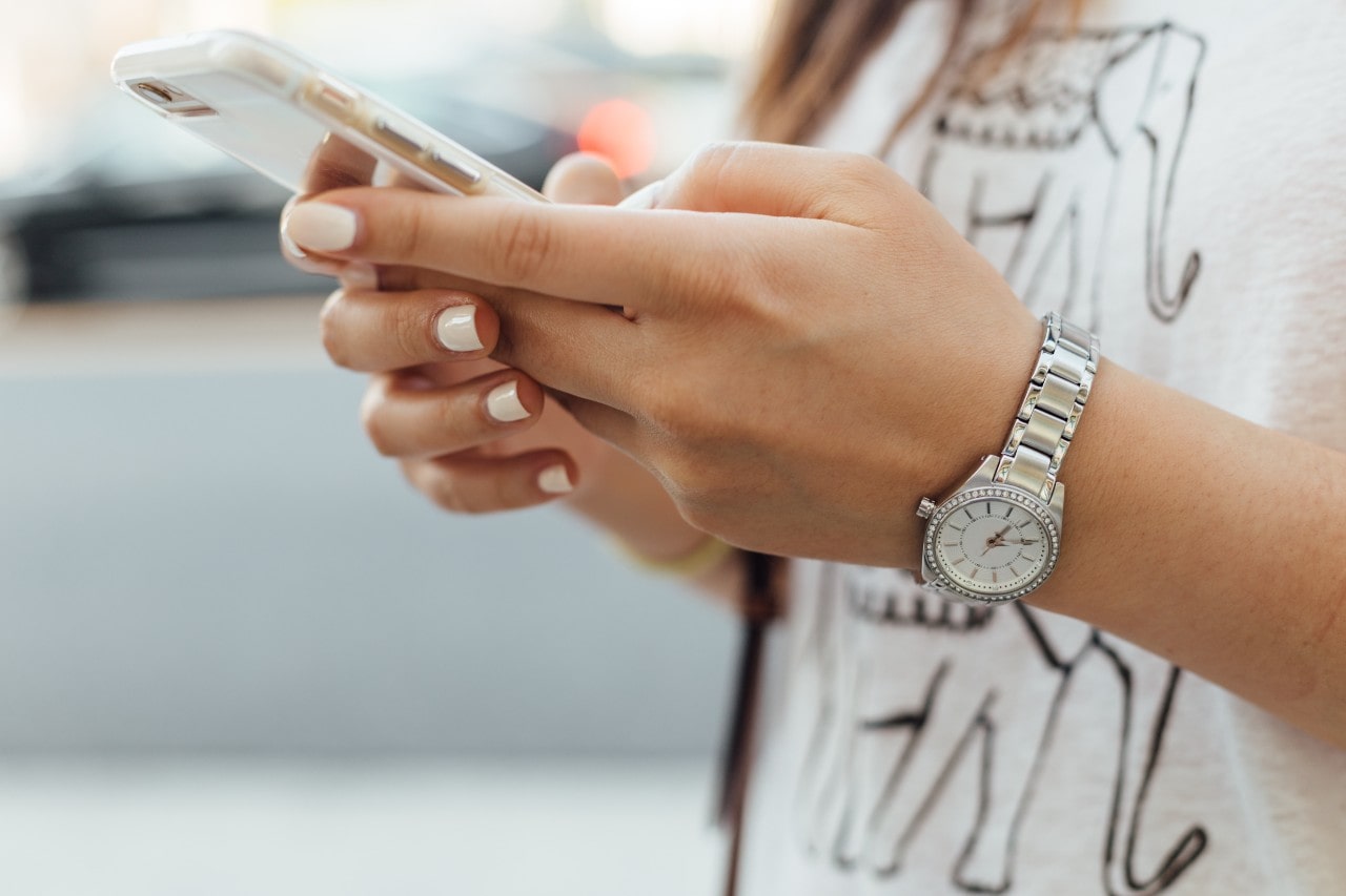 A closeup of a woman’s diamond watch as she texts on her cellphone.