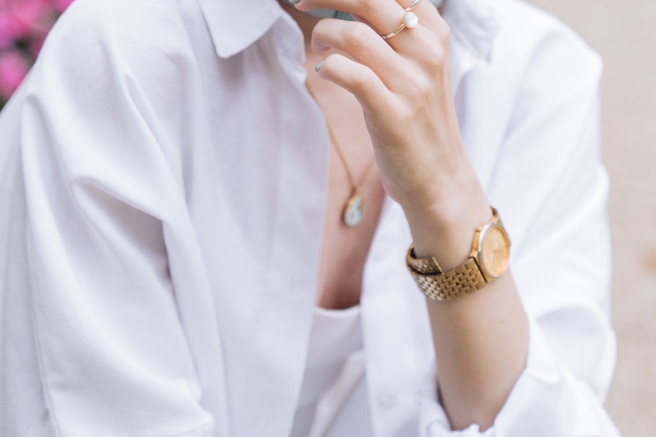 a woman in a white shirt wearing a yellow gold watch and reaching her hand to her face