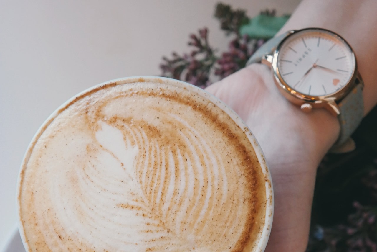 a hand wearing a minimalist watch holds a mug with a decorated latte.
