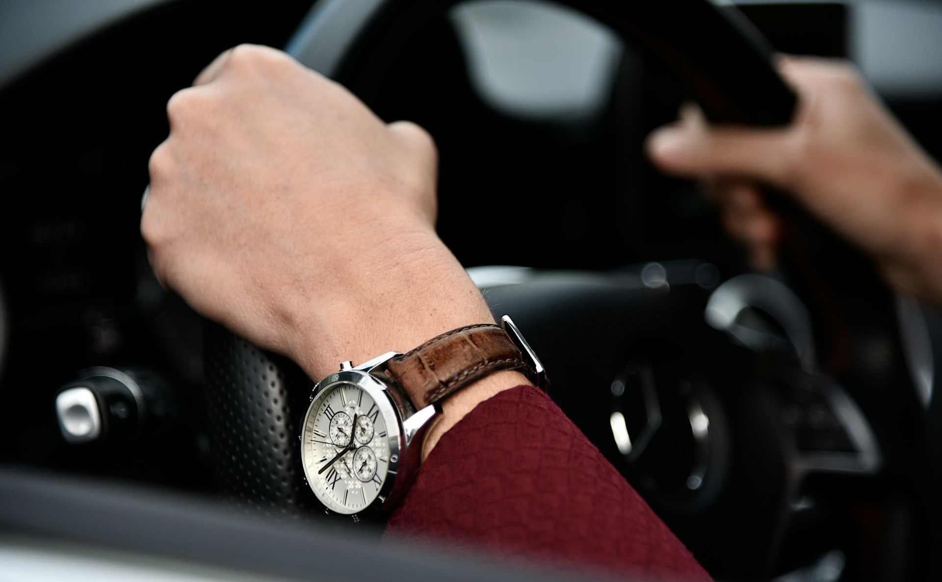 a close-up of a man’s hands holding a steering wheel, one wrist wearing a luxury watch