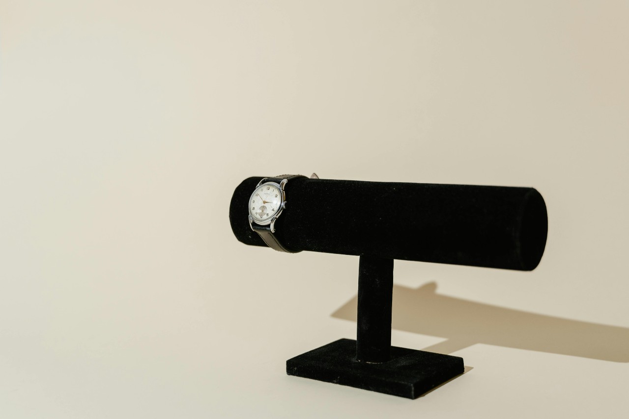 a silver and white watch on a black watch stand against a beige background