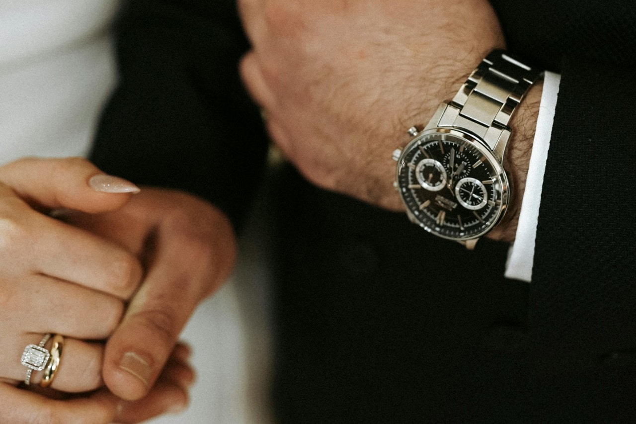 a bride and groom holding hands, the groom wearing a silver automatic watch