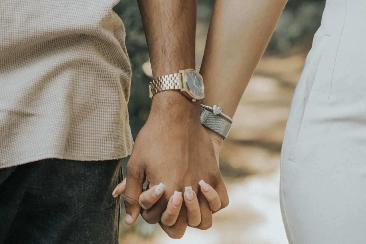 a couple holding hands, the man wearing a gold automatic watch