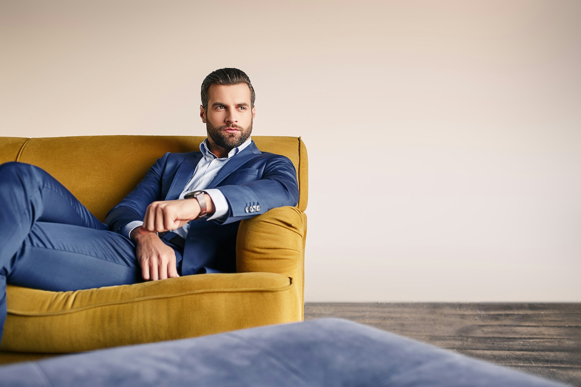 A well-dressed man lounging on a yellow sofa, wearing a luxury watch.