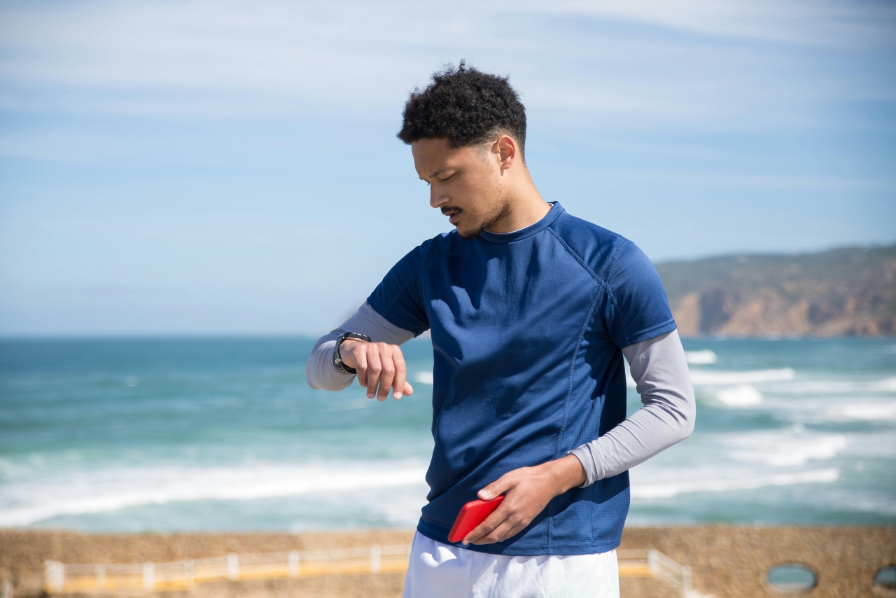 A young man at the beach checking his sports watch.