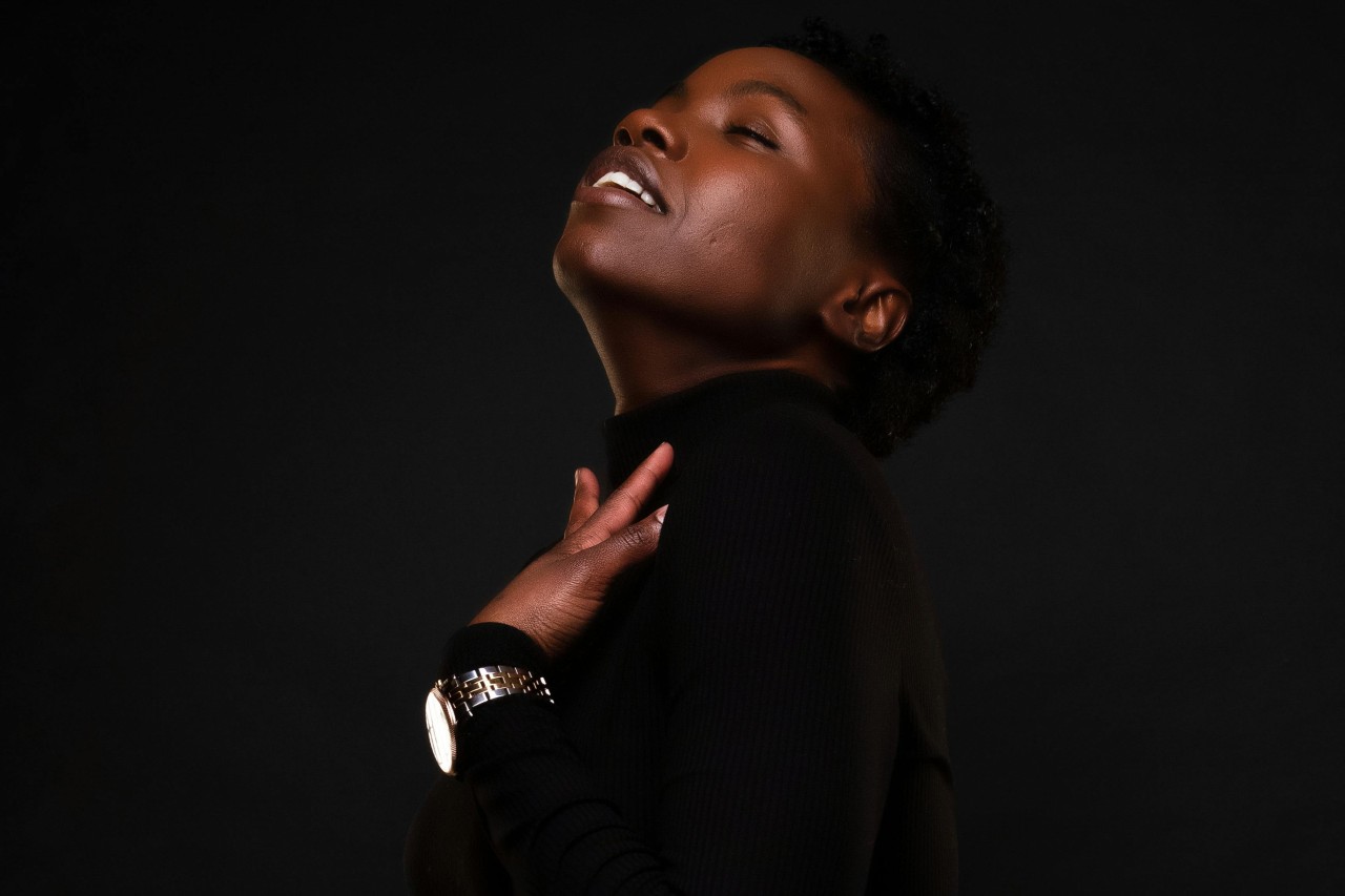 A woman dressed in all black against a black background, wearing a white and gold watch.