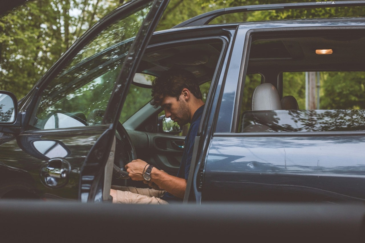 A casually dressed man in his car, wearing a fine watch.