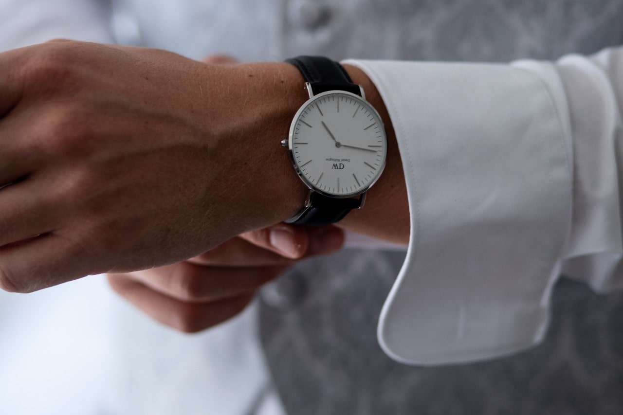 A well-dressed man putting an elegant, minimalist dress watch on his wrist.