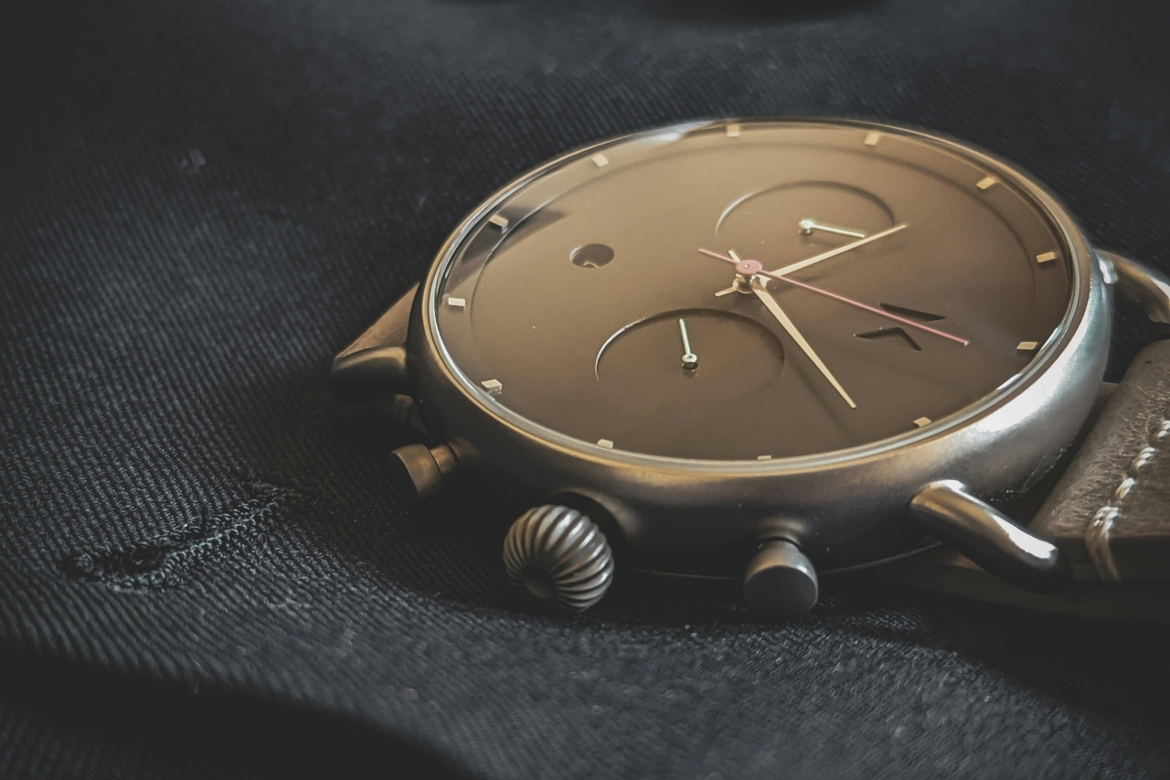 A close-up of a minimalist gold watch resting on a black jacket.