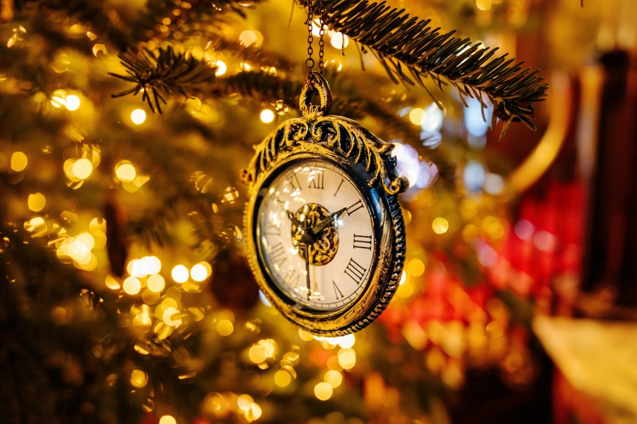 A close-up of a gorgeous pocket watch hanging off a branch of a shining Christmas tree.