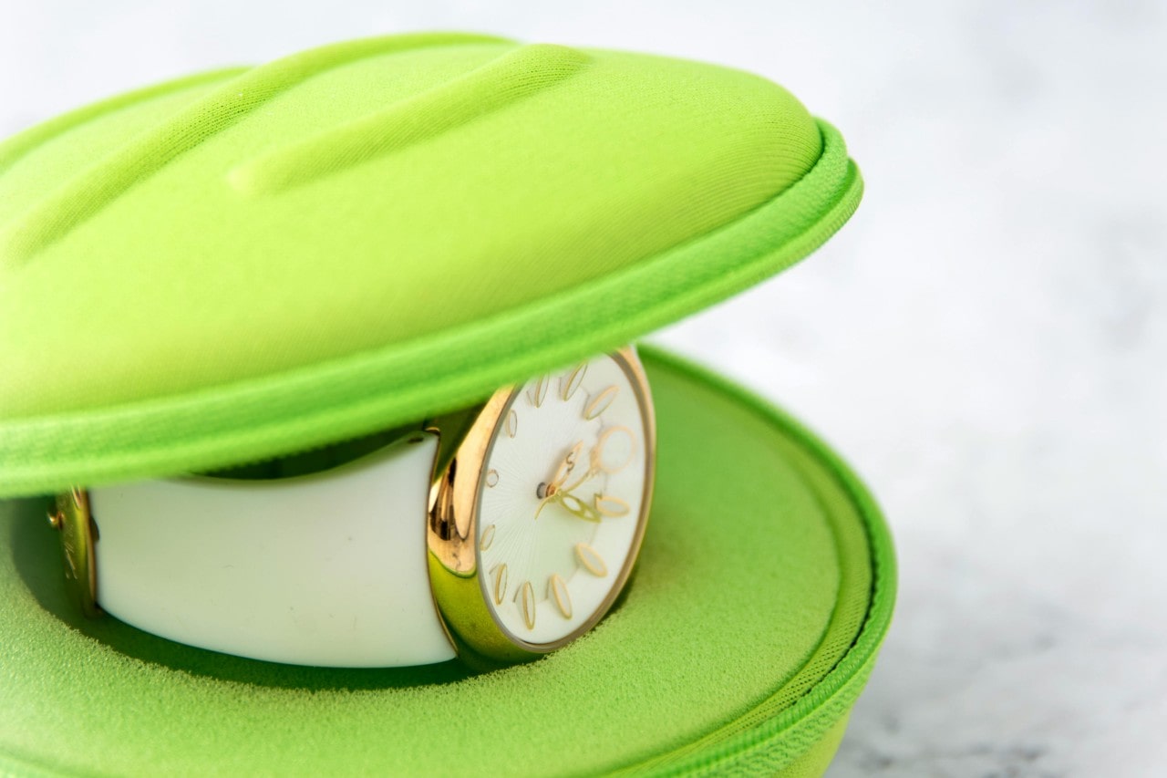 A close-up of a simple yet elegant all-white luxury watch with gold accents nestled inside a neon green clamshell case.