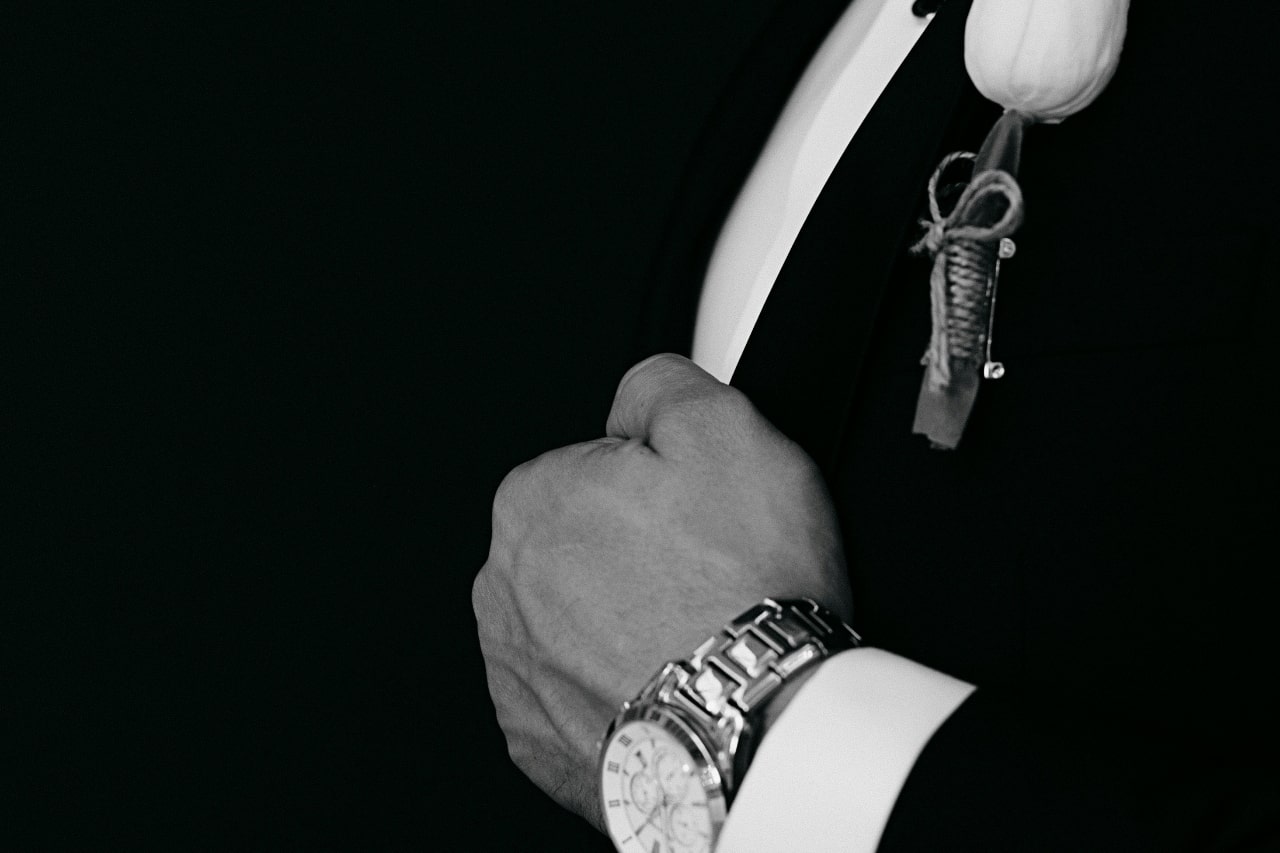 A close up of a groom adjusting his suit jacket.