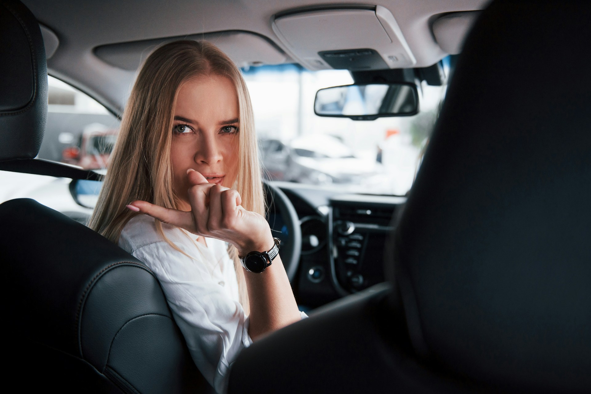 a lady driving a car and wearing a watch while pointing at the camera