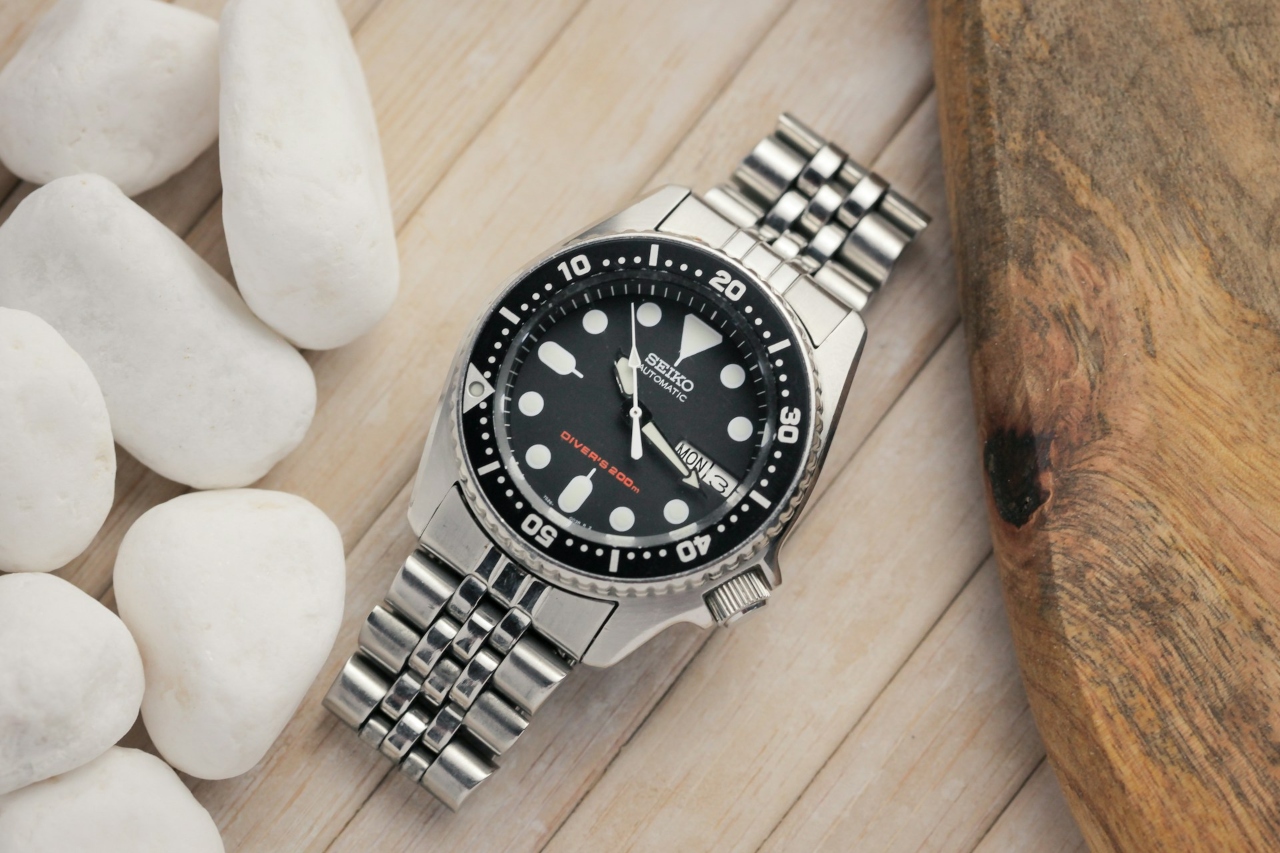 A close-up of a Seiko wristwatch on a wooden table, next to smooth decorative stones.