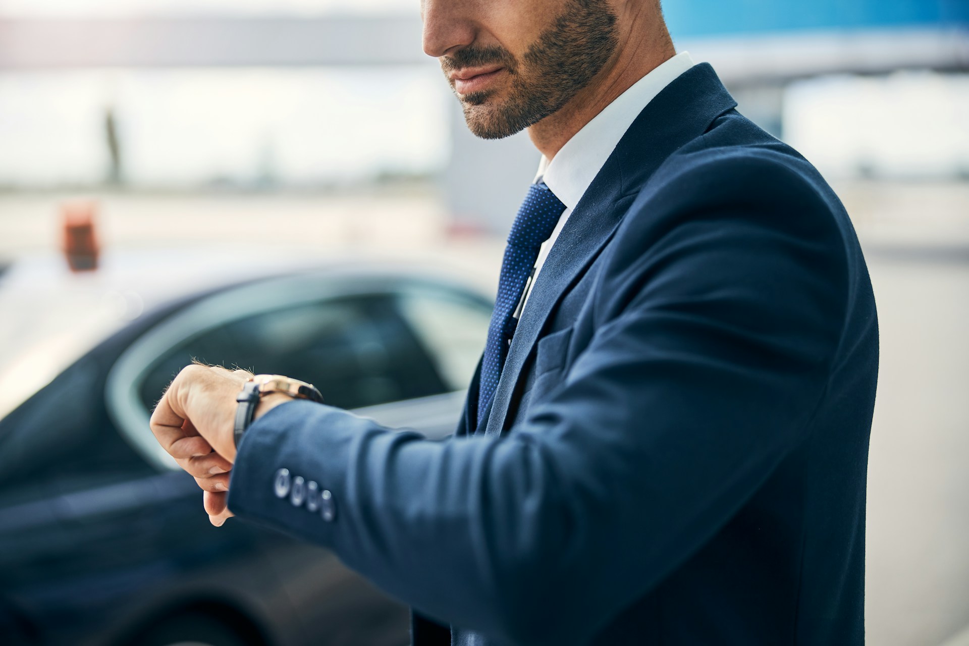 A man in a suit checking his watch as he stands by his car.