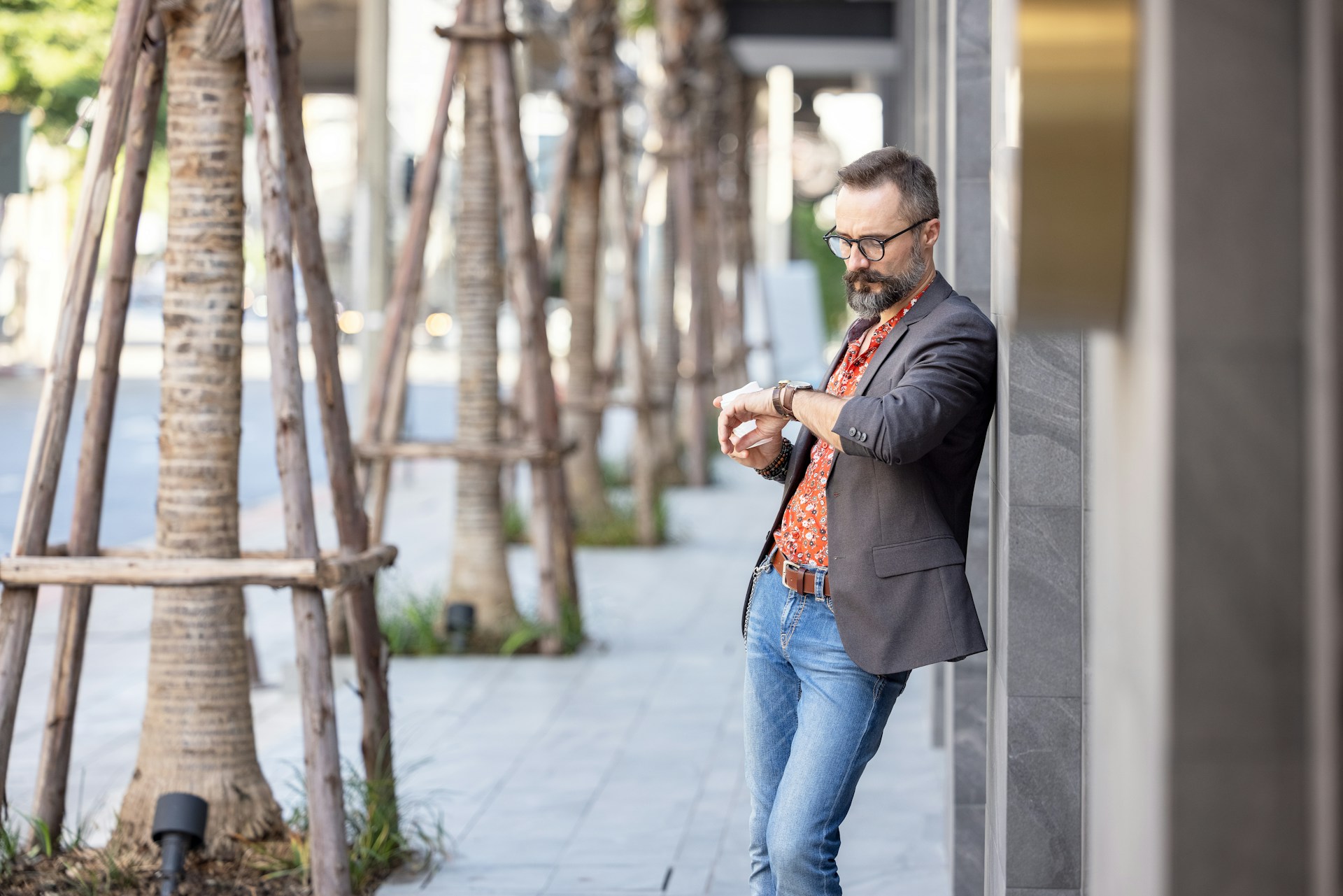 A man standing on the street looking at his watch.