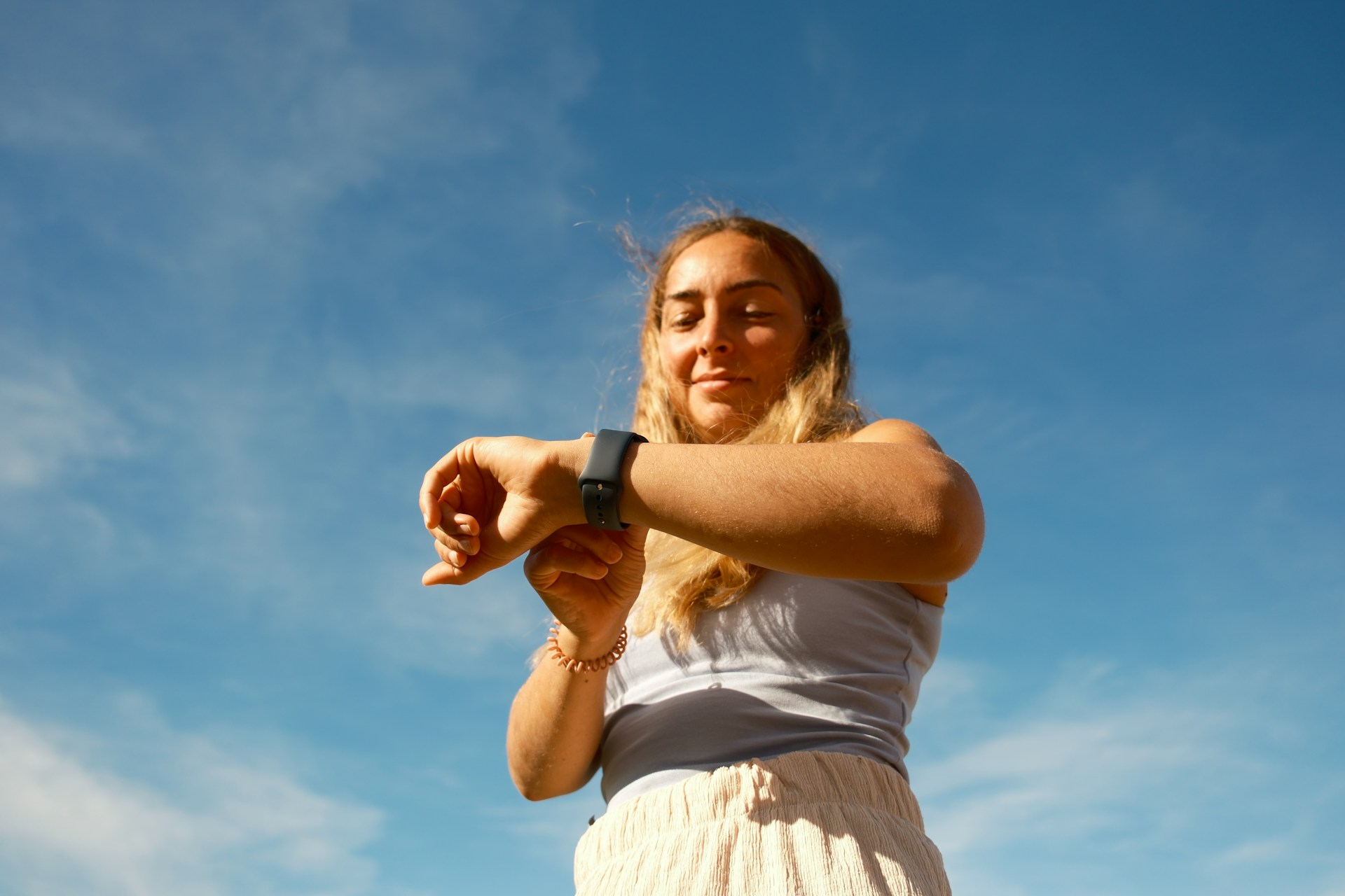 A low-angle view of a woman standing outside, checking her watch.