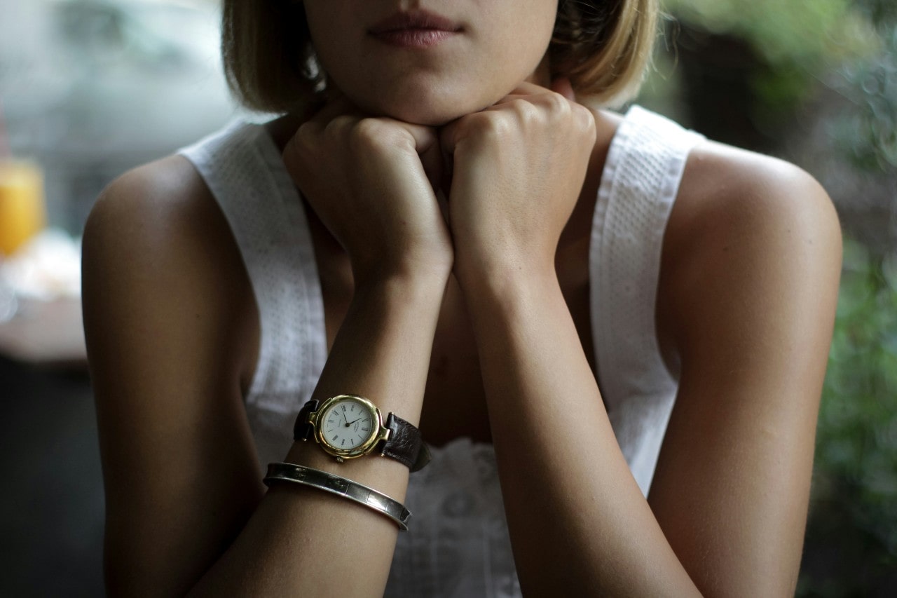 a woman posing with her hands under her chin, wearing a silver bangle and gold watch