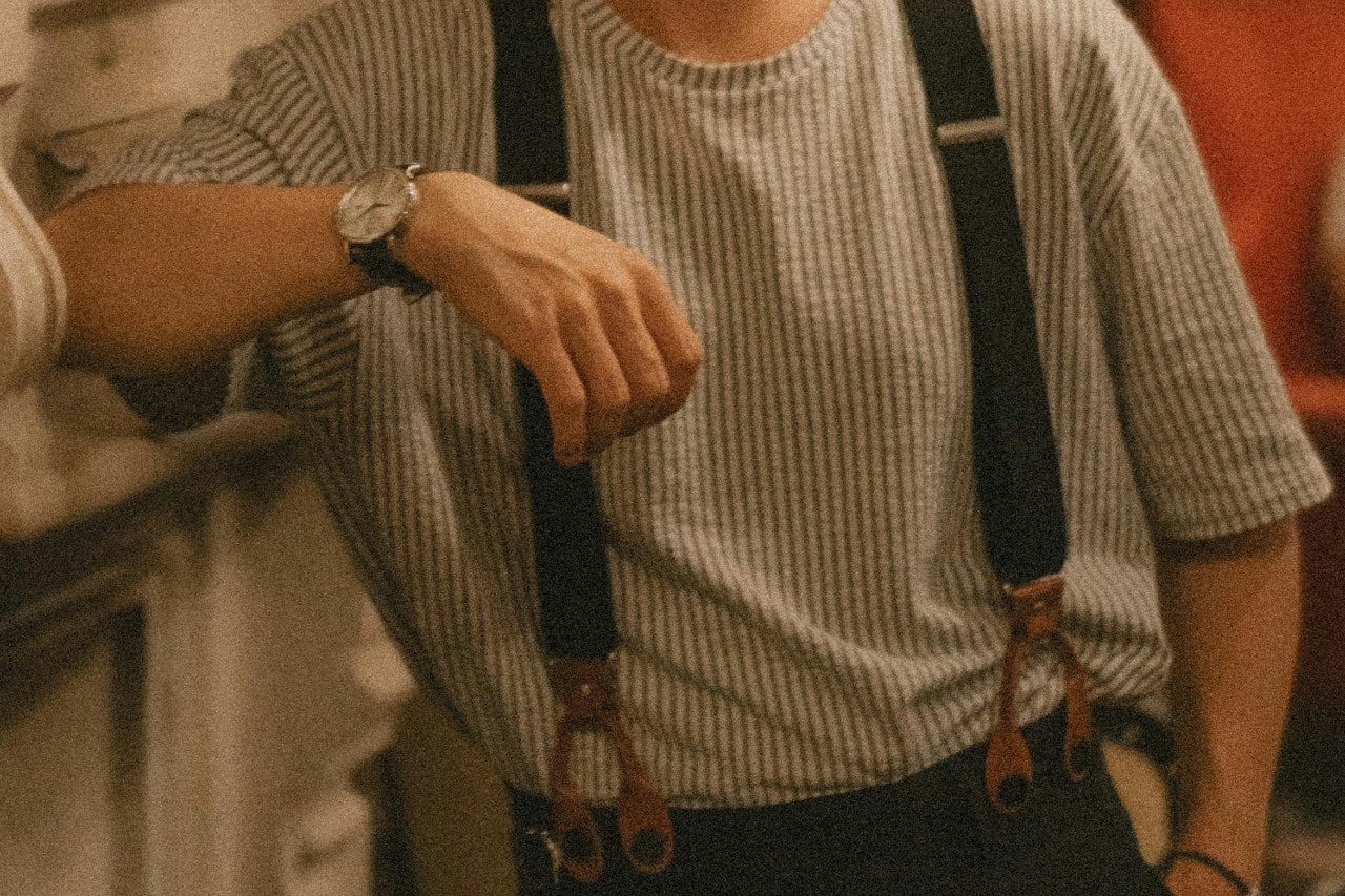 a man leaning on his elbow, wearing a silver watch and suspenders