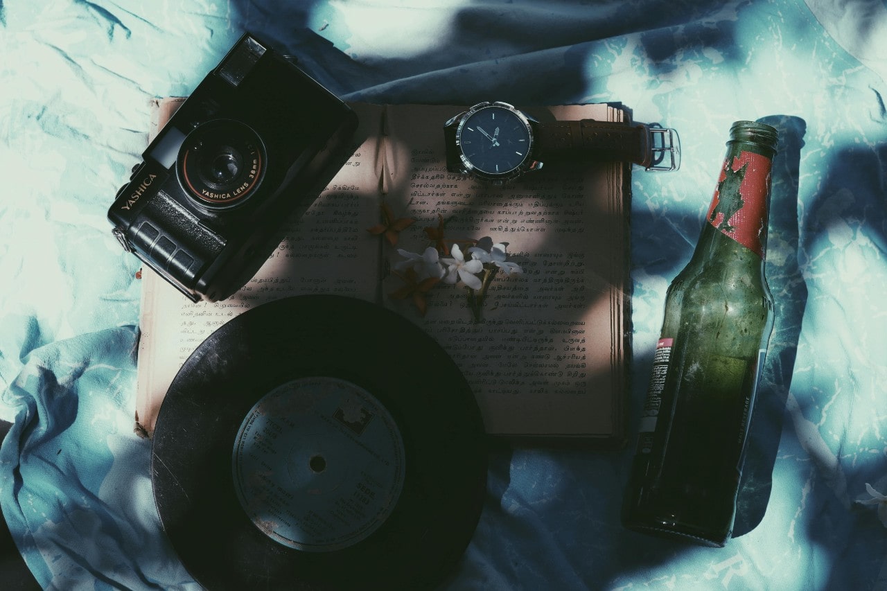 a wrist watch laid out on a book next to a record, camera, and glass bottle