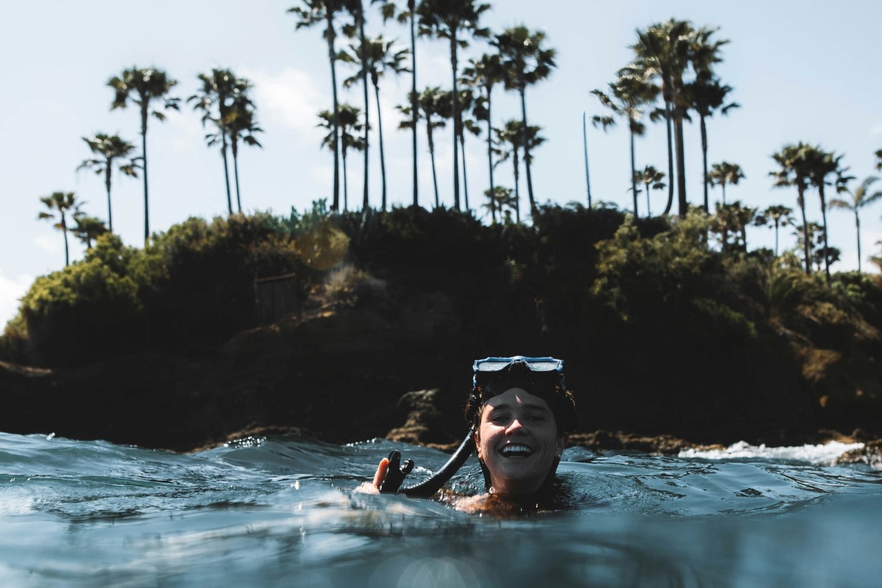 A woman wearing goggles goes swimming by an island.