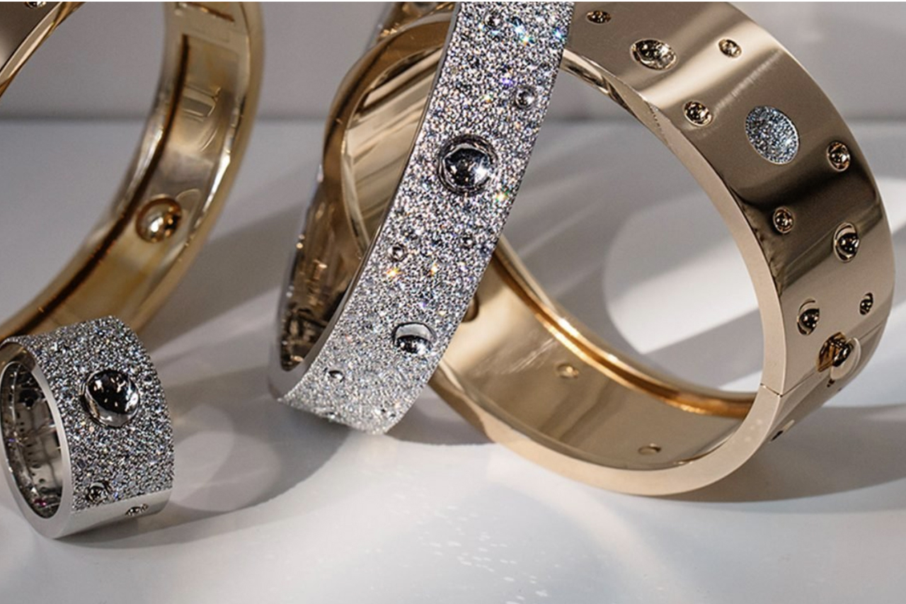 a line of white gold diamond eternity wedding bands being held between gloved fingers