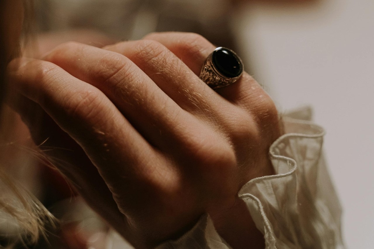 A close-up of a woman’s hand with an onyx ring on her pinky finger.