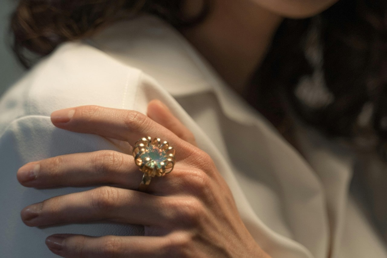 A woman’s hand, adorned with an opal fashion ring, resting on her shoulder.