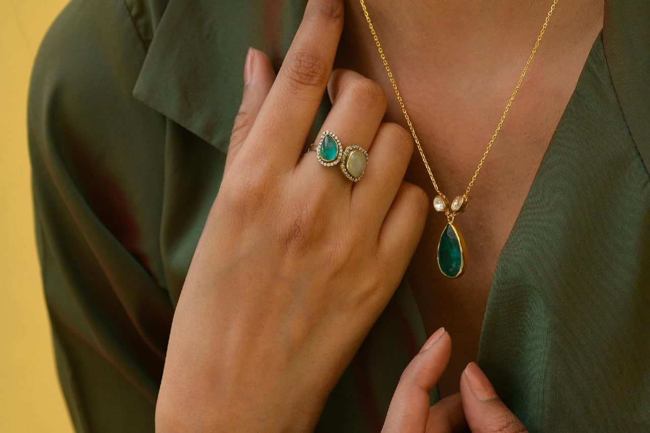 A woman wearing a toi et moi fashion ring and a green pendant necklace.