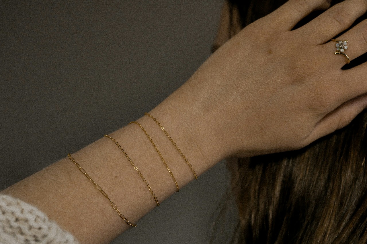 woman’s hand resting on her head, wearing four yellow gold bracelets and a fashion ring