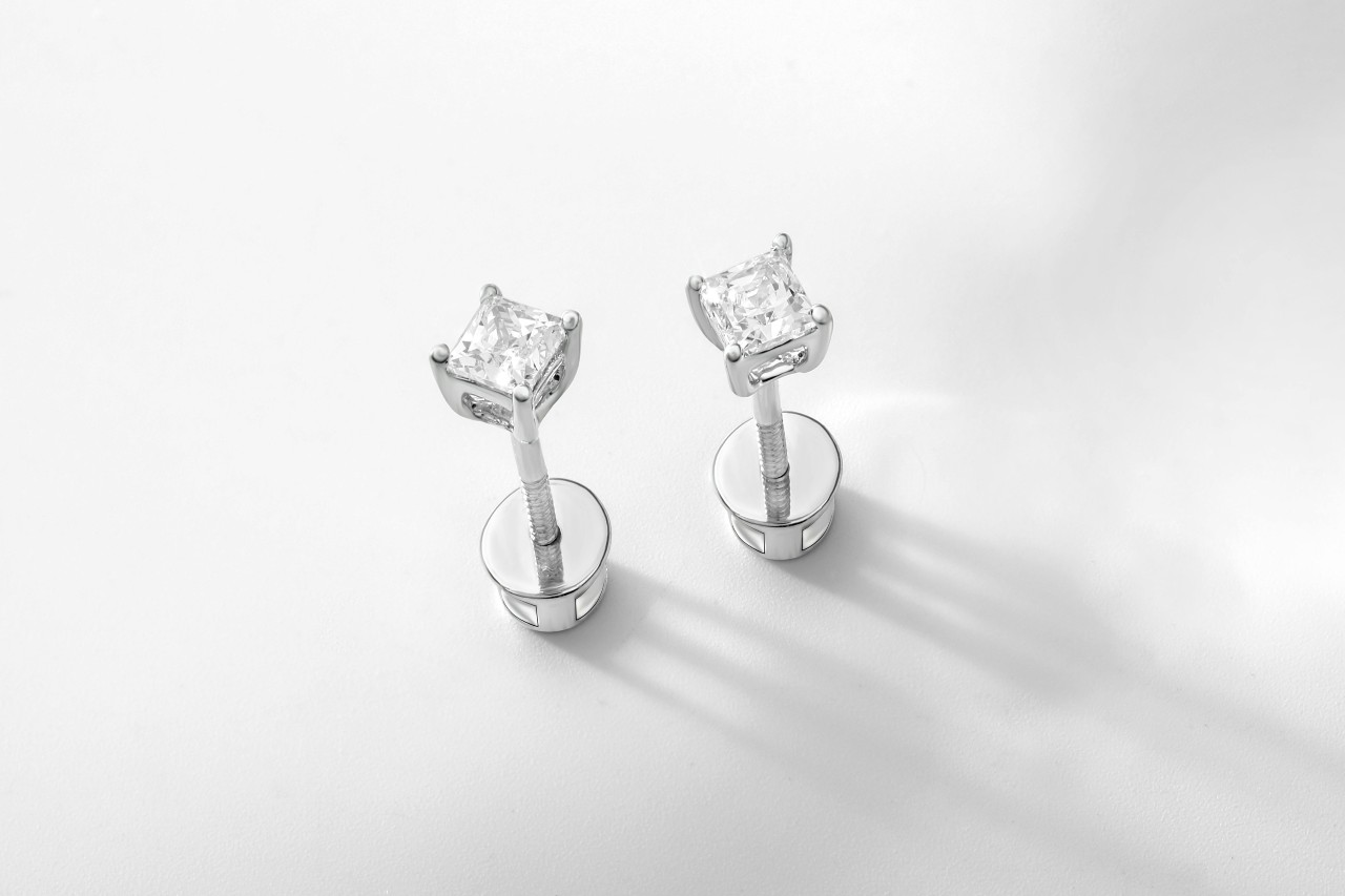 close up image of a pair of white gold princess cut diamond stud earrings on a white surface