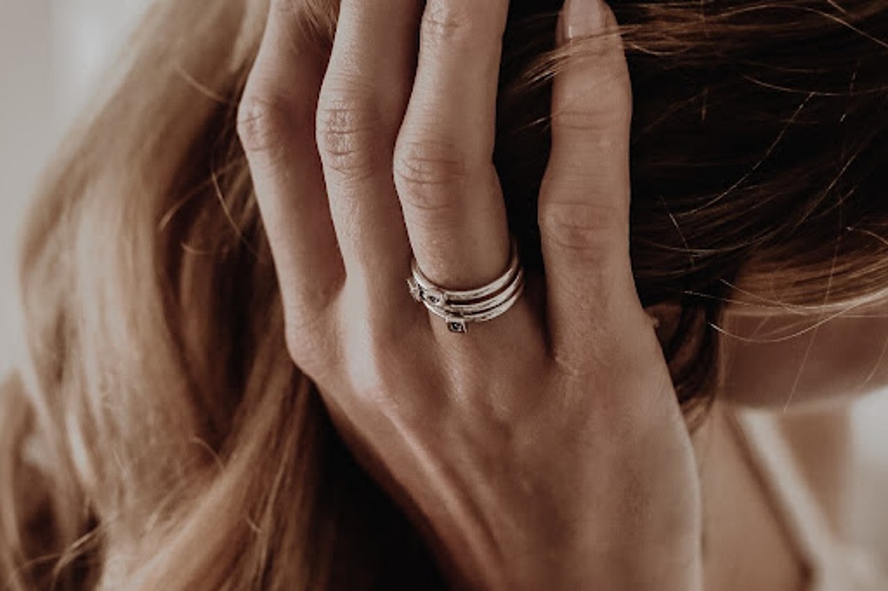 A close-up of a woman’s hand brushing her hair back, an ornate gold ring on her finger.