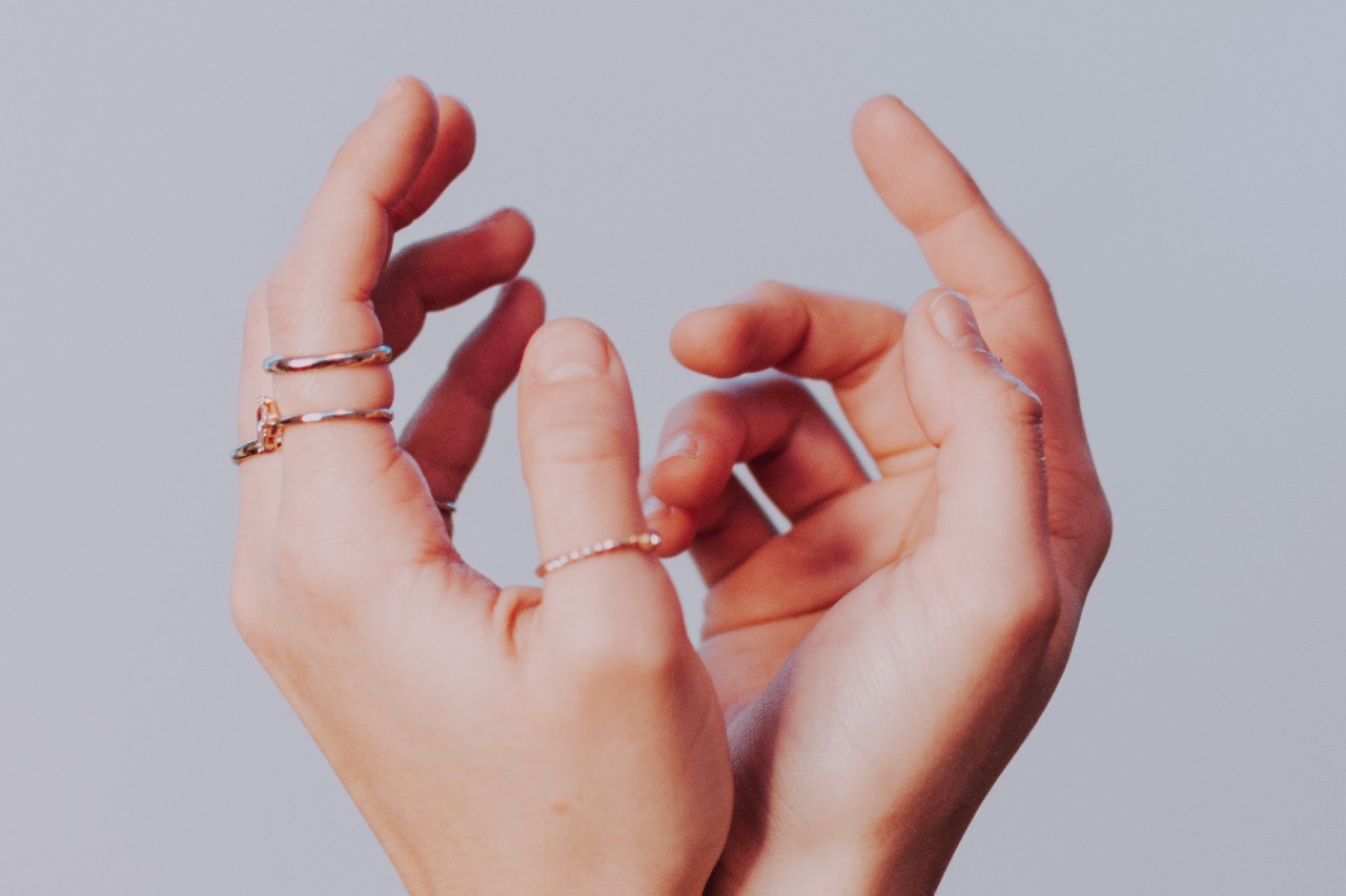 A close-up of a person’s hands adorned with delicate fashion rings.