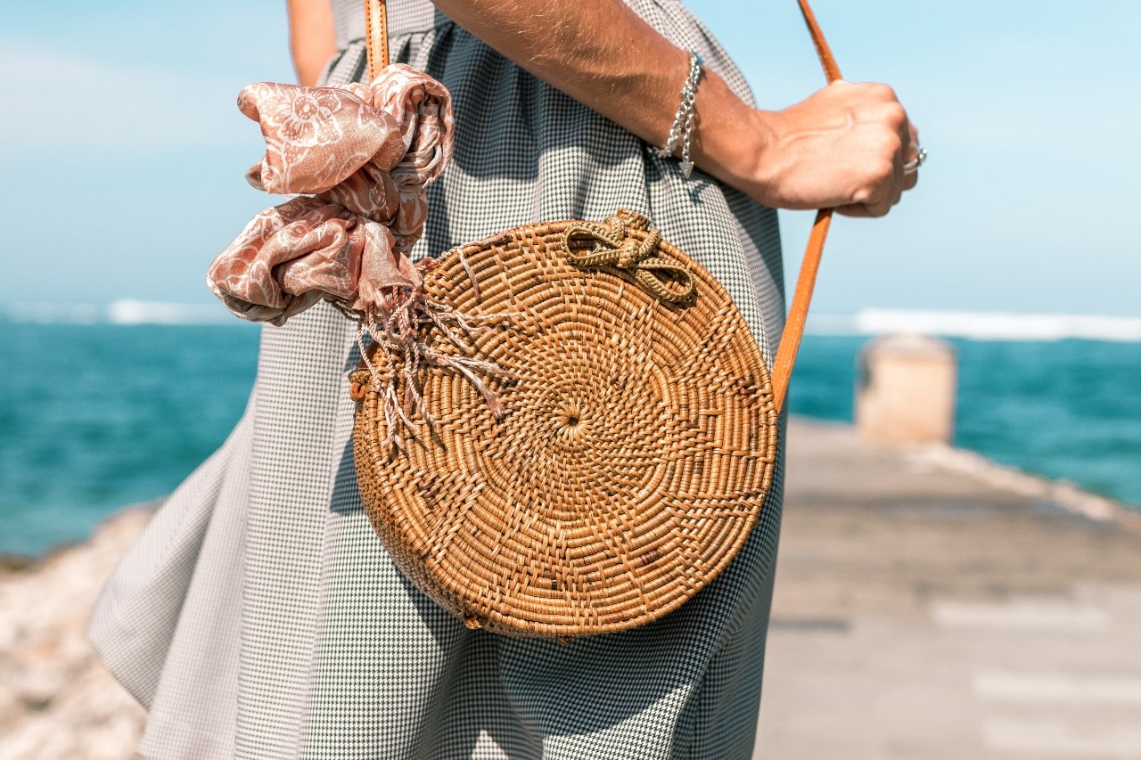 A woman at the beach holds her bag while wearing a bracelet. A woman at the beach holds her bag while wearing a bracelet.